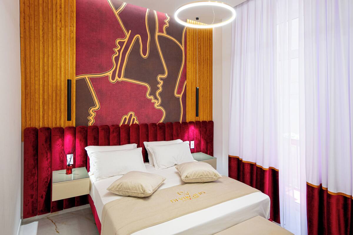 Une chambre moderne avec un grand lit, un banc, une table de chevet et une œuvre d’art accrochée au mur.