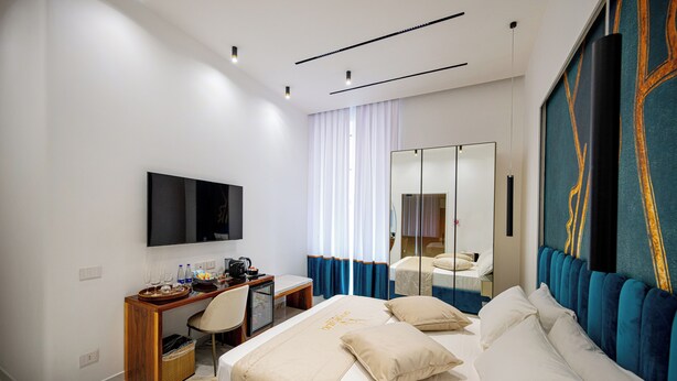 Ein modernes Hotelzimmer mit einem großen Bett, einem Schreibtisch mit Stuhl, einem Flachbildfernseher und einem großen Spiegel.