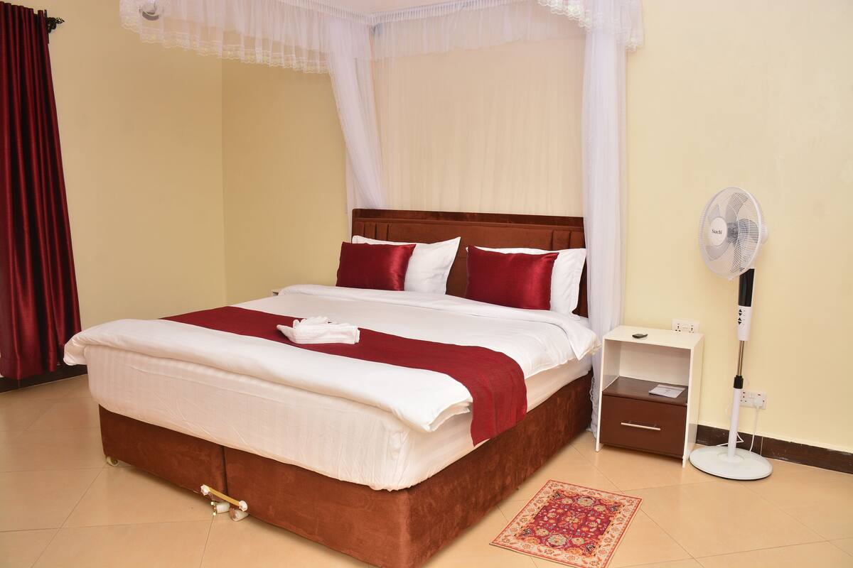 A neatly made bed with a white and red bedspread, a bedside table with a fan, and a small drawer unit.