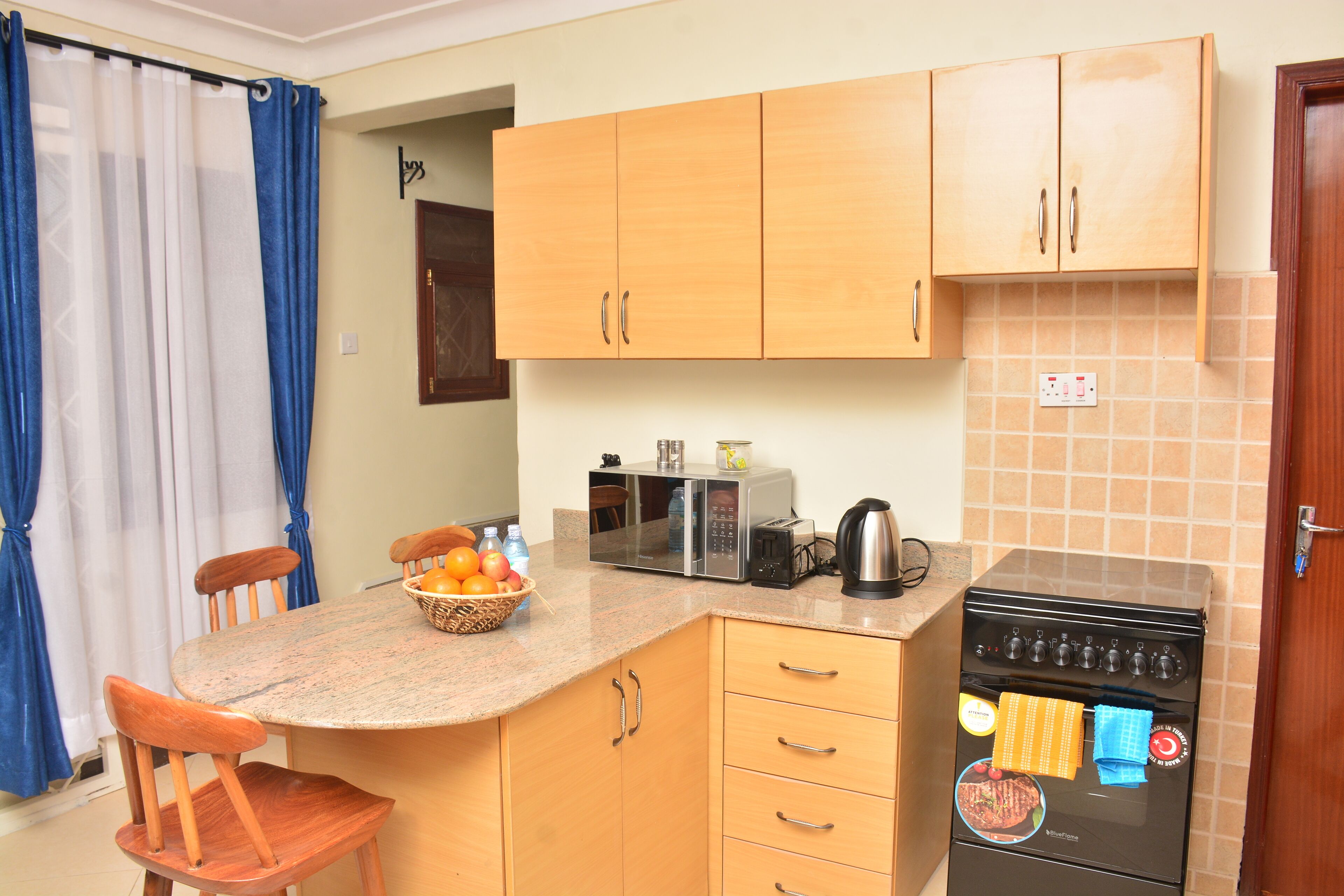 A kitchen with wooden cabinets, a microwave, a kettle, and a stove.