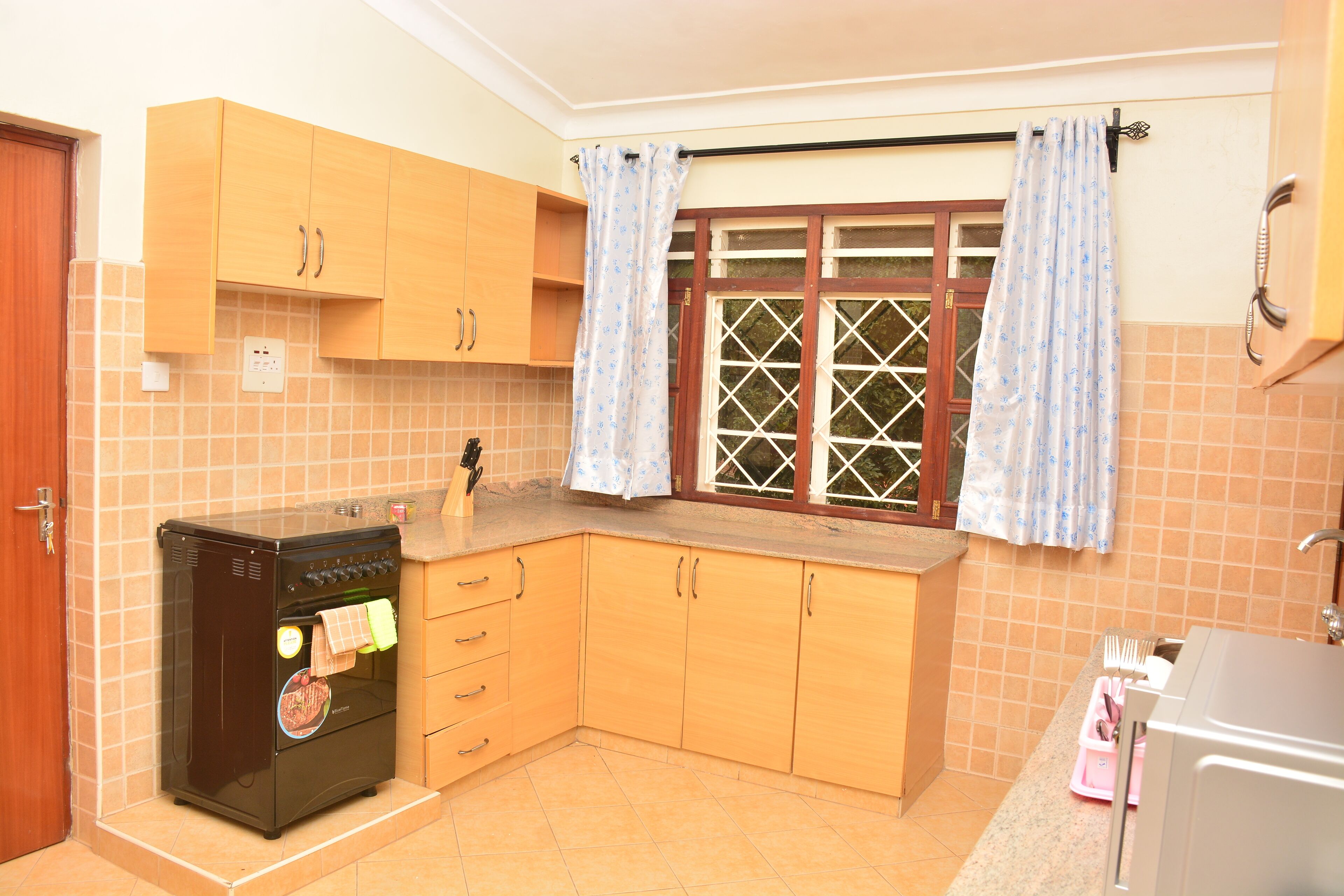 A kitchen with wooden cabinets, a built-in oven, a window with curtains, and a sink.