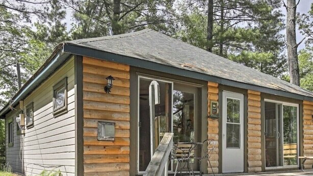 Une cabane en rondins avec un porche, des marches en bois et un petit espace de détente extérieur.