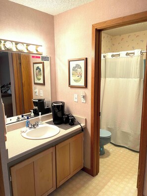 A bathroom with a sink, mirror, coffee maker, and a shower curtain. - Morning Tee Times  Walk to Golf  Summer Stay (Mancelona)