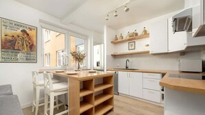 A modern kitchen with white cabinets, a wooden island, and a dining area with white chairs. - Cozy Apartment | 2 Balconies | Work Space (Wrocław)