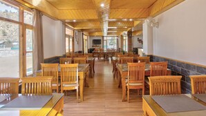 Un vaste espace dédié à la salle à manger, avec des tables et des chaises en bois, de grandes fenêtres et un mur décoratif en pierre.