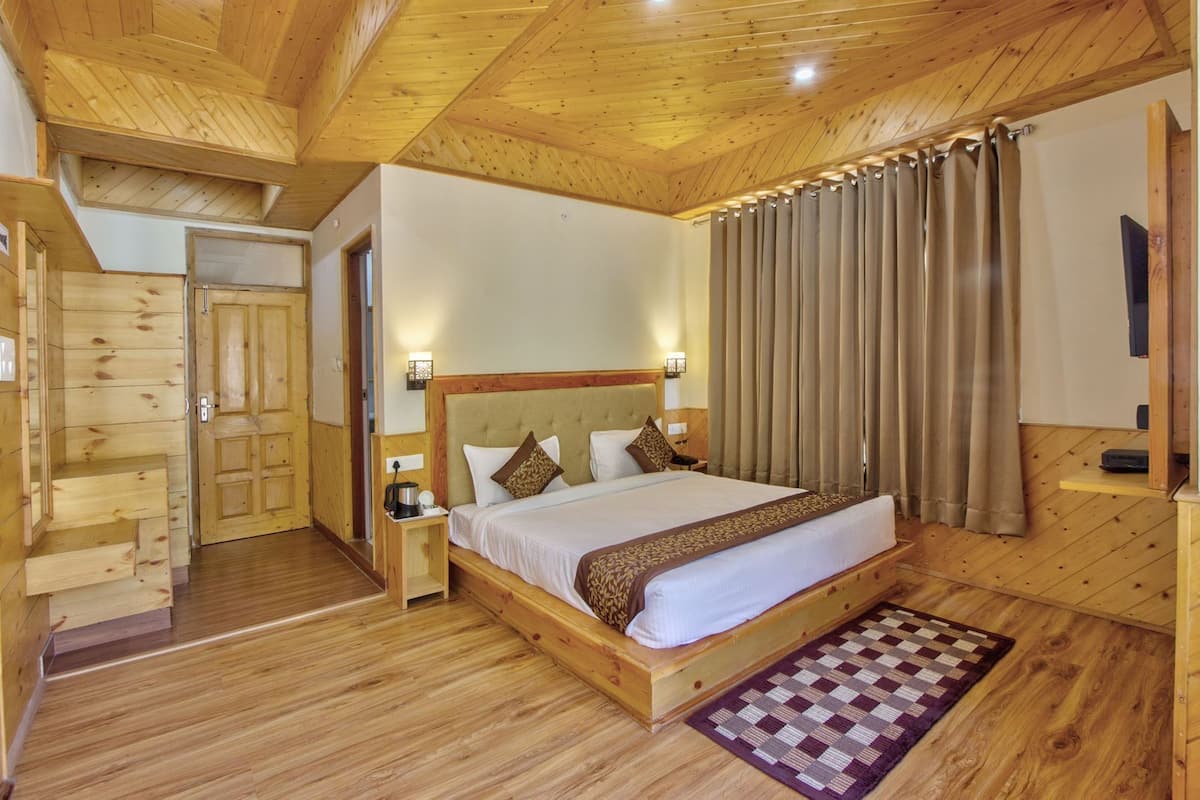 Une chambre à coucher aux murs lambrissés, avec un grand lit, une table de chevet, une lampe fixée au mur et un tapis à carreaux.