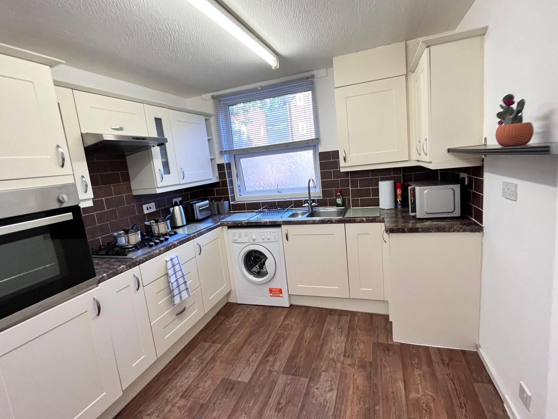 A compact kitchen with a washing machine, microwave, and a small window.