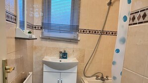 A bathroom with a sink, toilet, shower, and a window with blinds. - Hive Stays Close to Abbeywood Free Parking Wifi (Erith)
