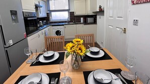 A compact kitchen with a dining table set for four, a washing machine, and a microwave. - Hive Stays Close to Abbeywood Free Parking Wifi (Erith)
