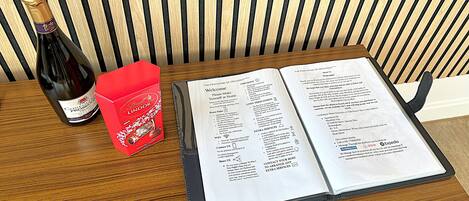 A wooden table with a bottle of wine, a red box, and an open menu.