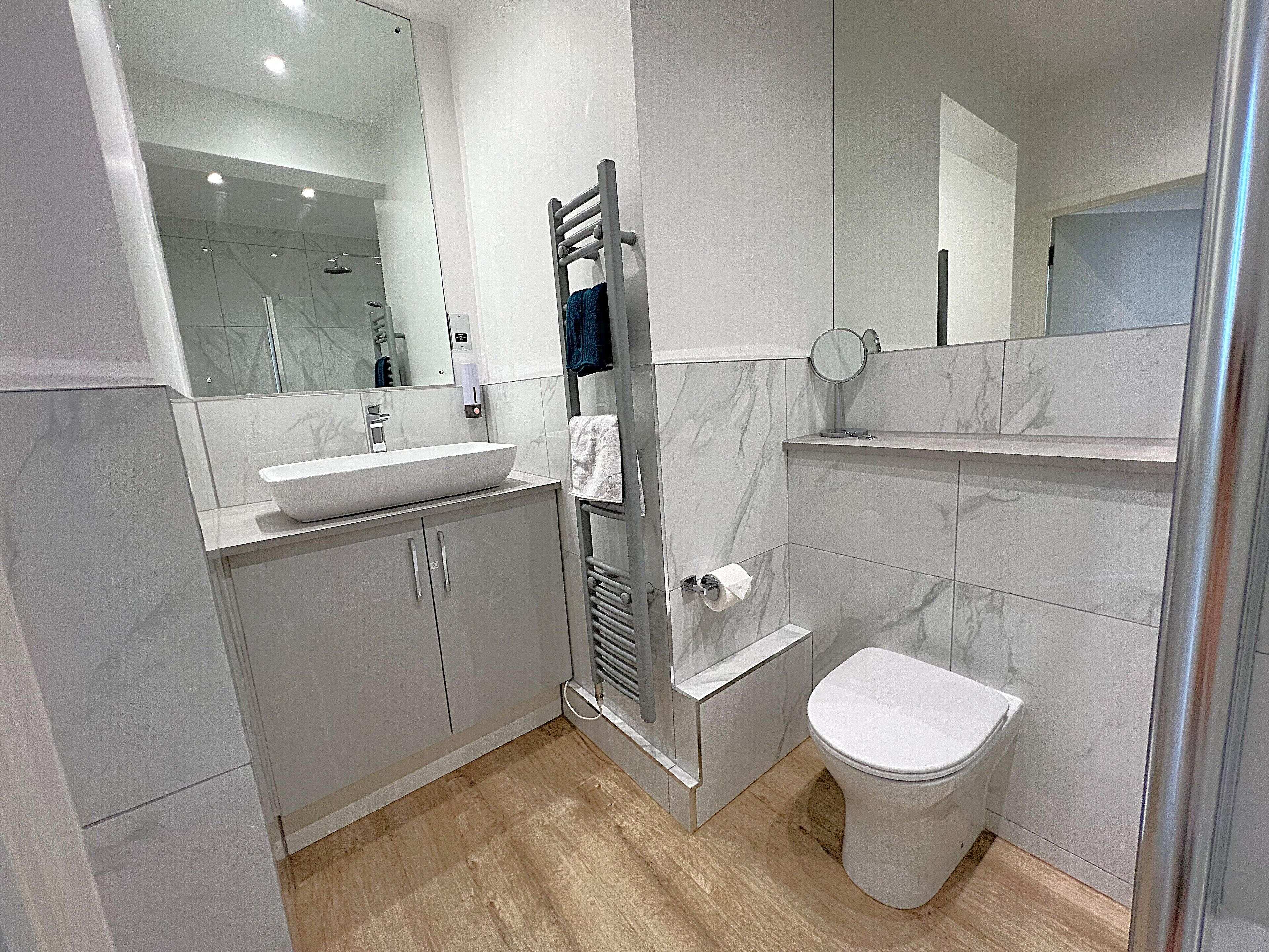 A modern bathroom with a large mirror, a sink, a toilet, and a shower area.