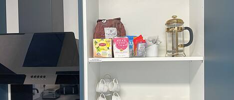 A kitchenette with a coffee machine, a shelf with coffee pods, tea bags, and a coffee pot.