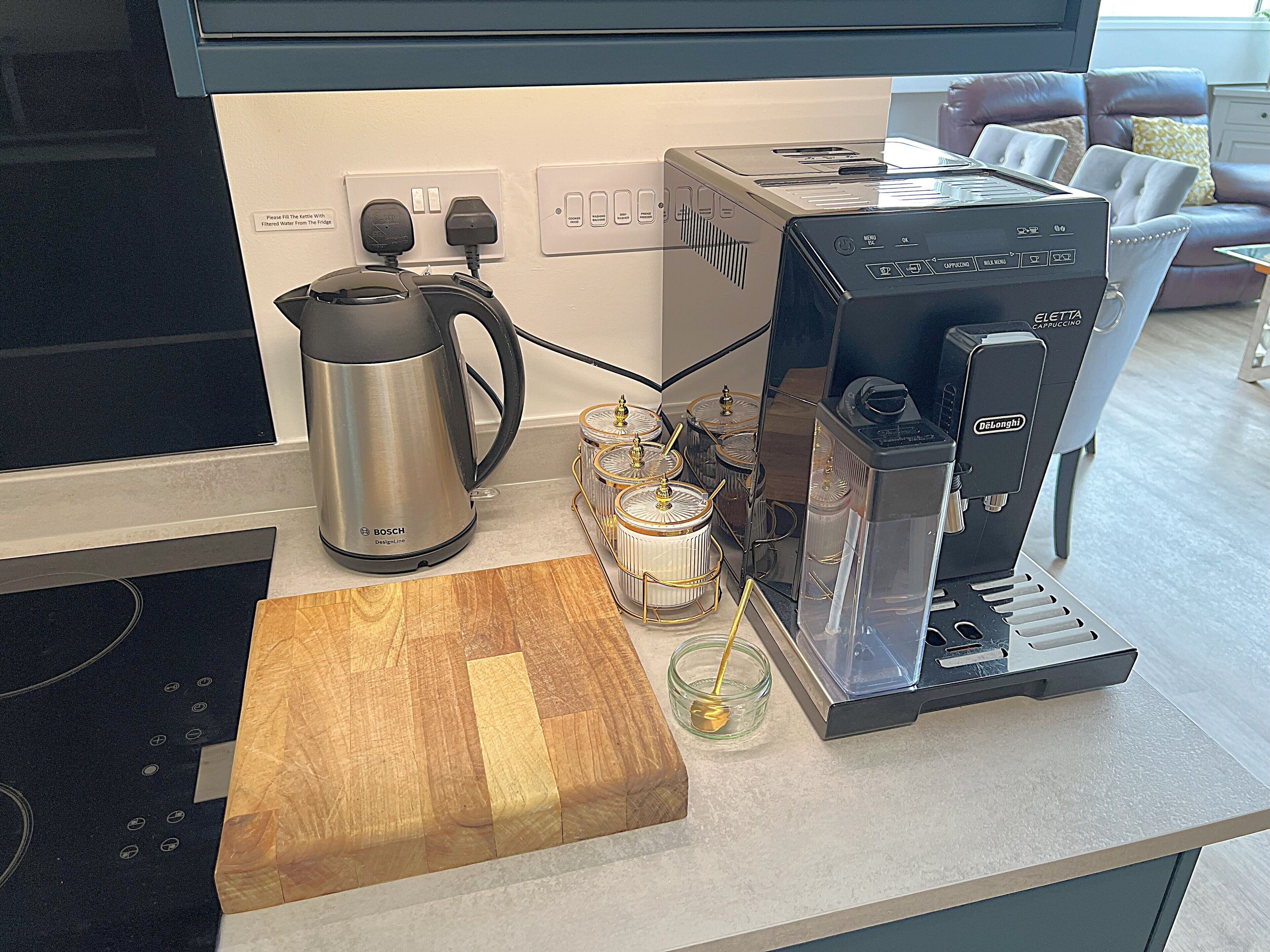 A kitchen with a Bosch kettle, a Delonghi espresso machine, and a wooden cutting board.