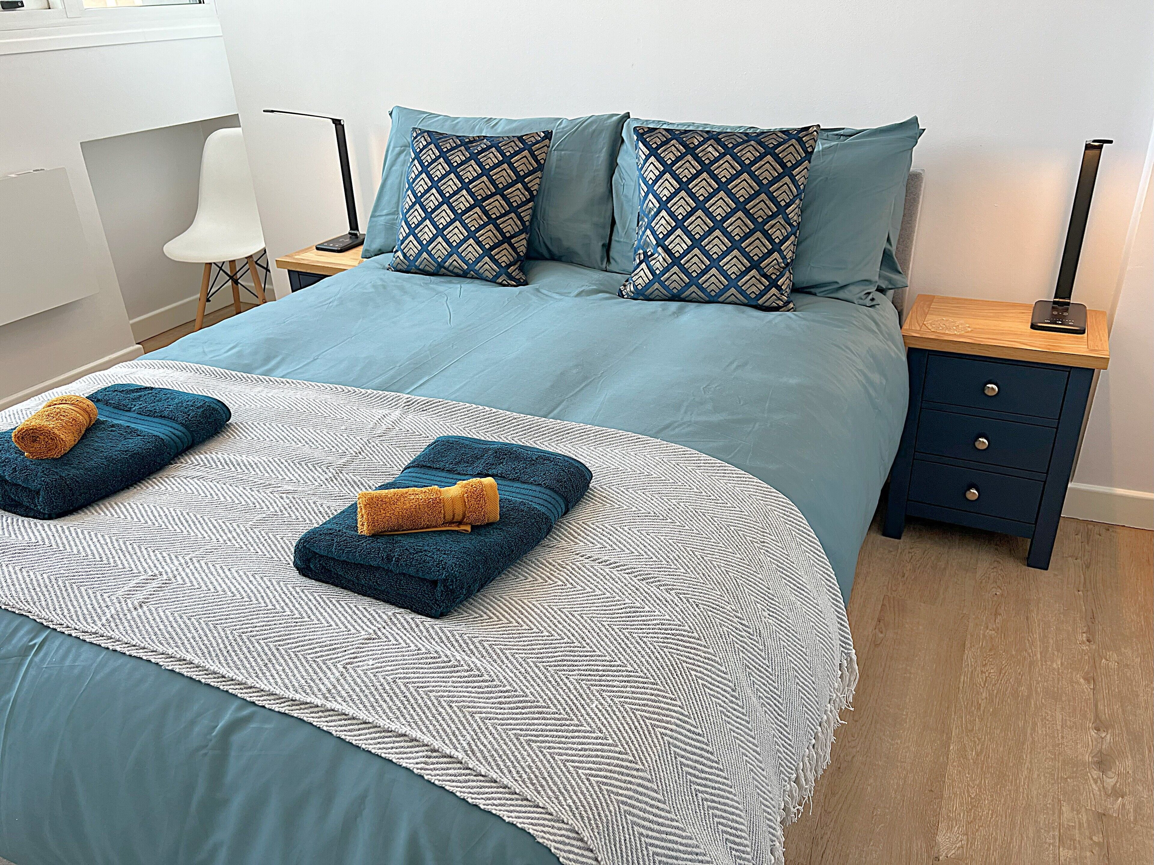 A neatly made bed with a patterned bedspread, two pillows, and two folded towels.