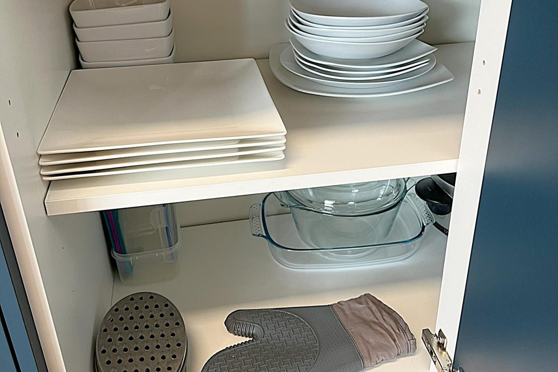 A kitchen with white cabinets, a stack of white plates, a glass baking dish, and a gray oven mitt.