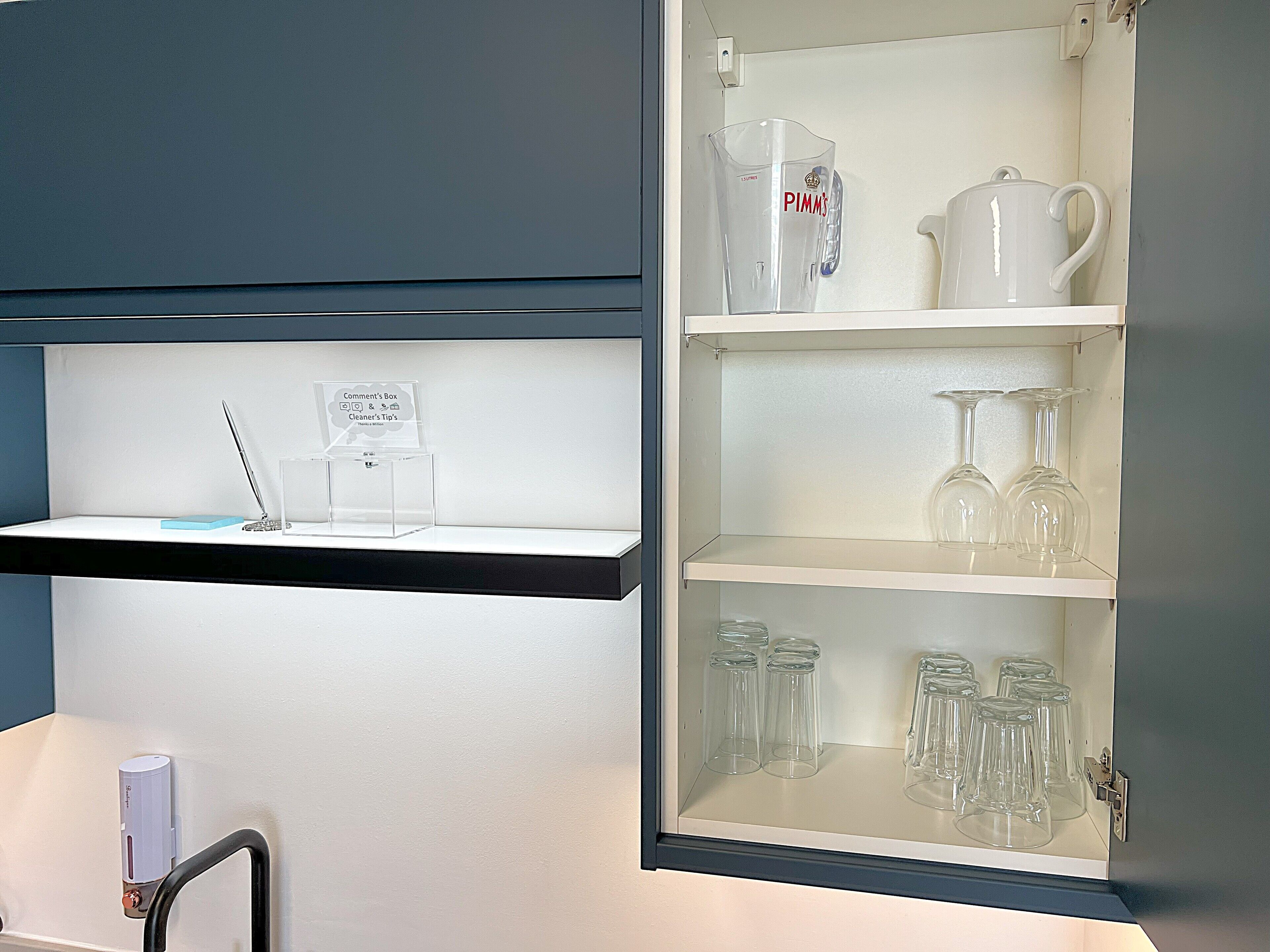 En minibar med en genomskinlig behållare i glas, en vit kanna och flera vinglas.