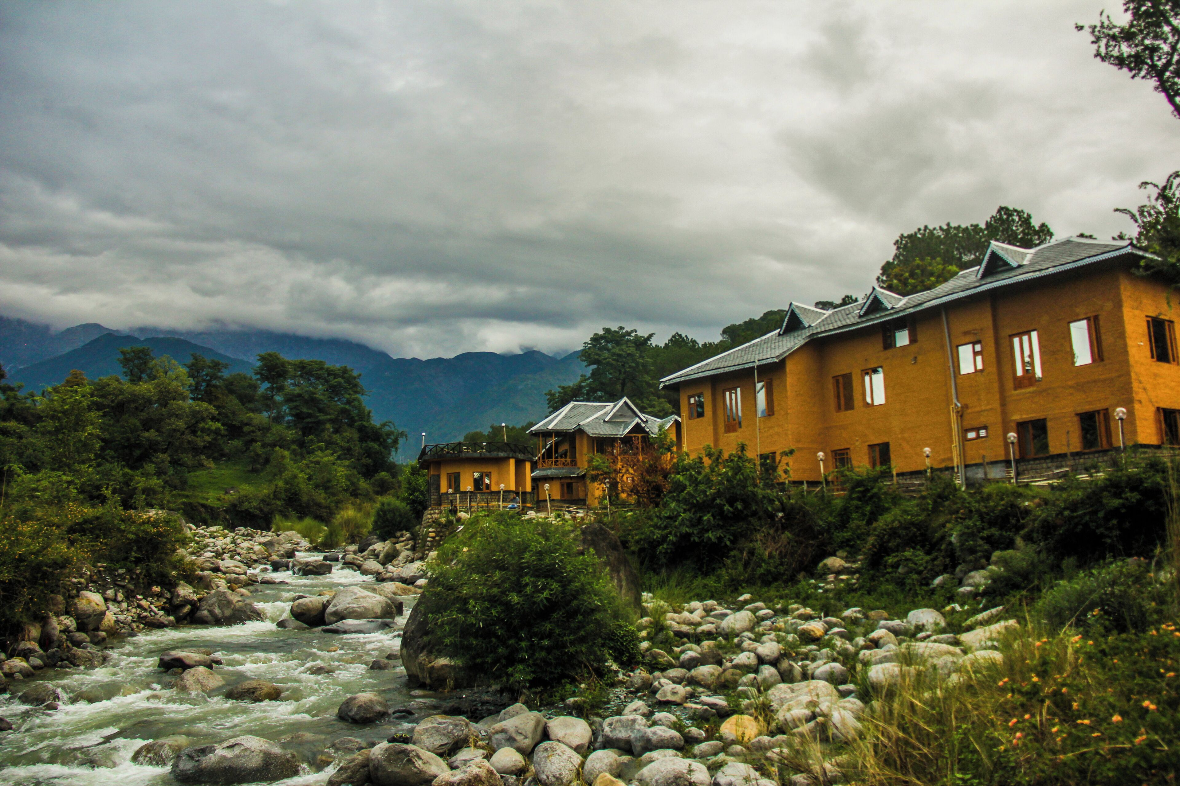 Un hotel a orillas de un río, con varias edificaciones, un lecho rocoso y montañas al fondo.