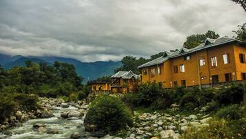 Un hotel a orillas de un río, con varias edificaciones, un lecho rocoso y montañas al fondo.