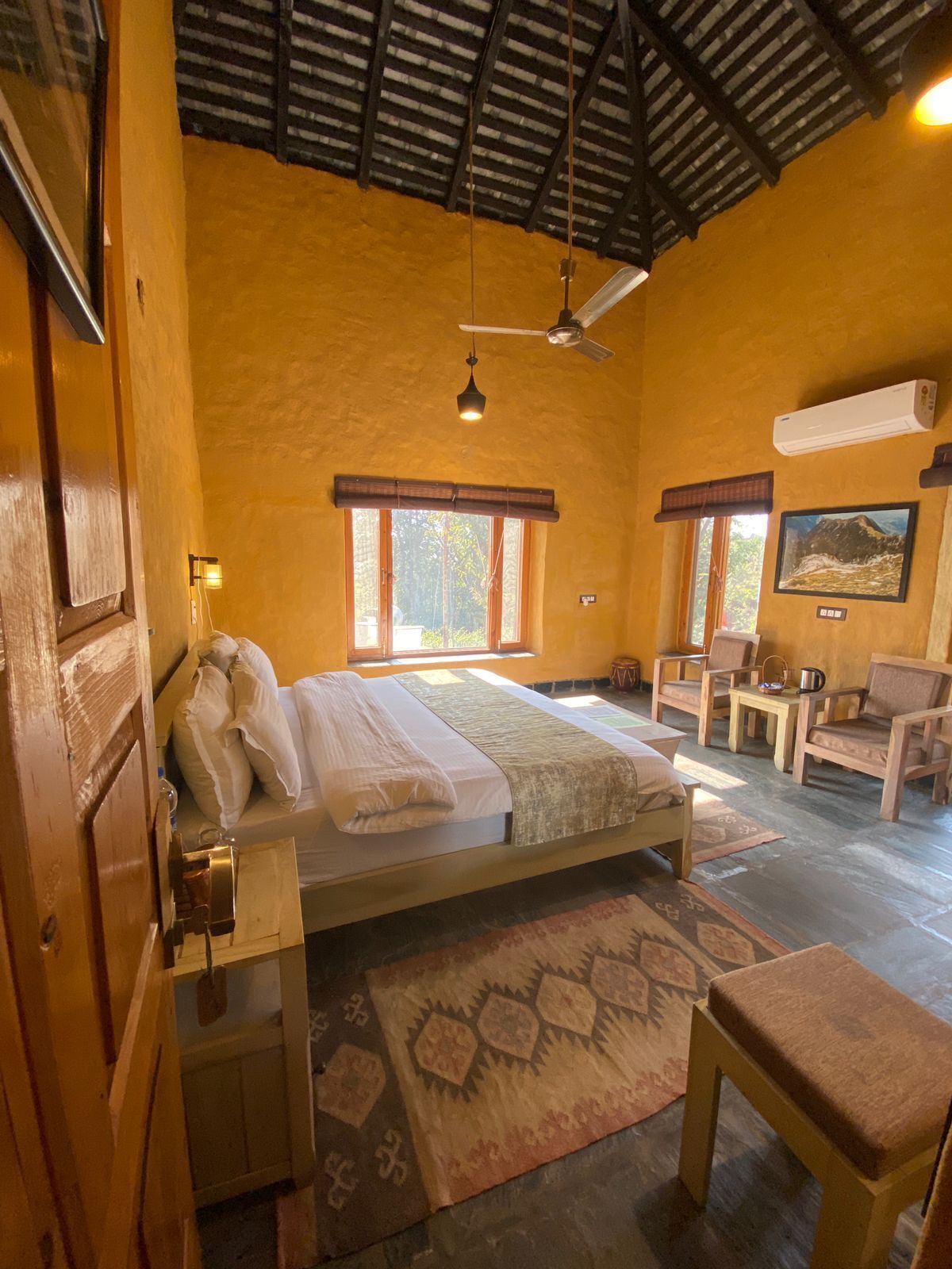 Um quarto com cama, ventilador de teto, janela, cadeira e mesa.