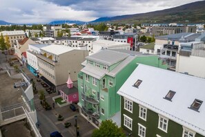 A town with various buildings, including a green multi-story building with a pink tower, and a white building with a sign. - Hafnarstræti 100, Downtown Apartment (Akureyri)