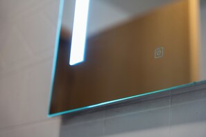 A bathroom with a mirror, a light fixture, and a power button symbol. - Hafnarstræti 100, Downtown Apartment (Akureyri)