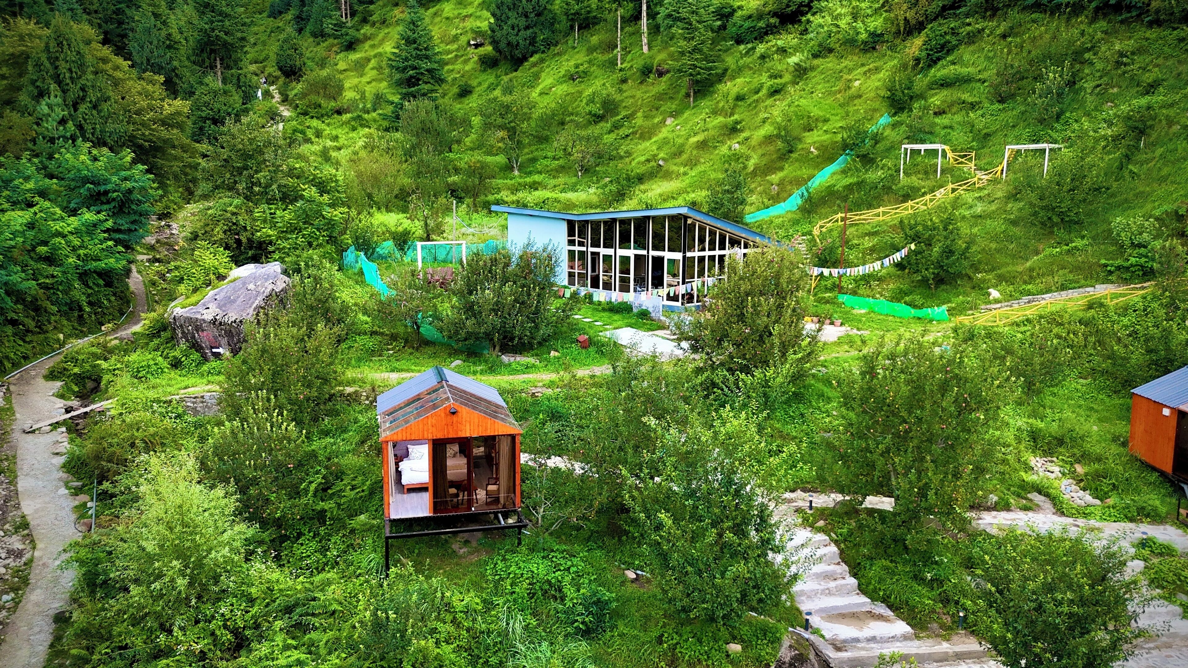 A hillside hotel with a central building surrounded by lush greenery, a small guesthouse, and a winding path.
