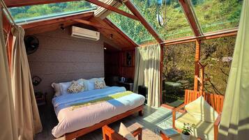 Ein gemütliches Schlafzimmer mit einem großen Bett, Holzbalkendecke und Blick auf üppiges Grün.