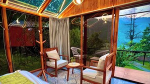 Ein gemütliches Zimmer mit einem großen Bett, zwei Holzstühlen, einem kleinen Tisch und Bergblick durch große Fenster.