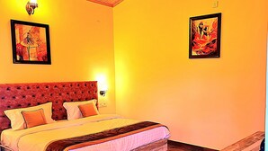 A bedroom with a large bed, a wooden headboard, two wall-mounted lamps, and two framed artworks. - Prashanti Farms & Resort (Dehradun)