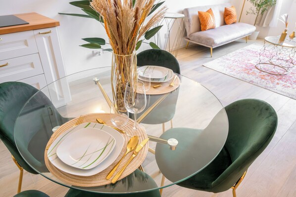 Uma área de jantar moderna com mesa de vidro, cadeiras verdes e um vaso com plantas secas.