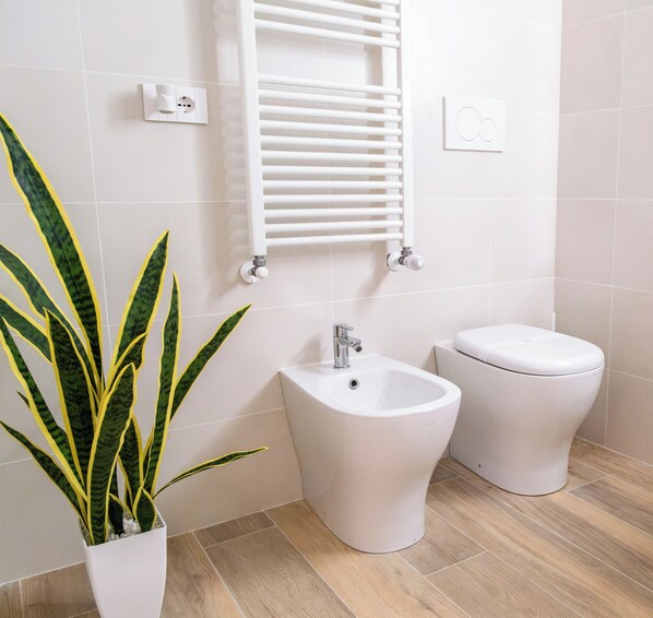 Un baño con bidé, inodoro y una planta en maceta.