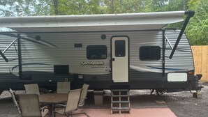 En autocamper med et spiseområde, der inkluderer et bord og stole, et overdækket picnicbord og en stige til adgang.
