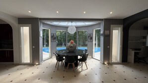 Un comedor moderno con mesa y sillas de vidrio, un centro de mesa decorativo y vistas a una piscina a través de grandes puertas de vidrio.