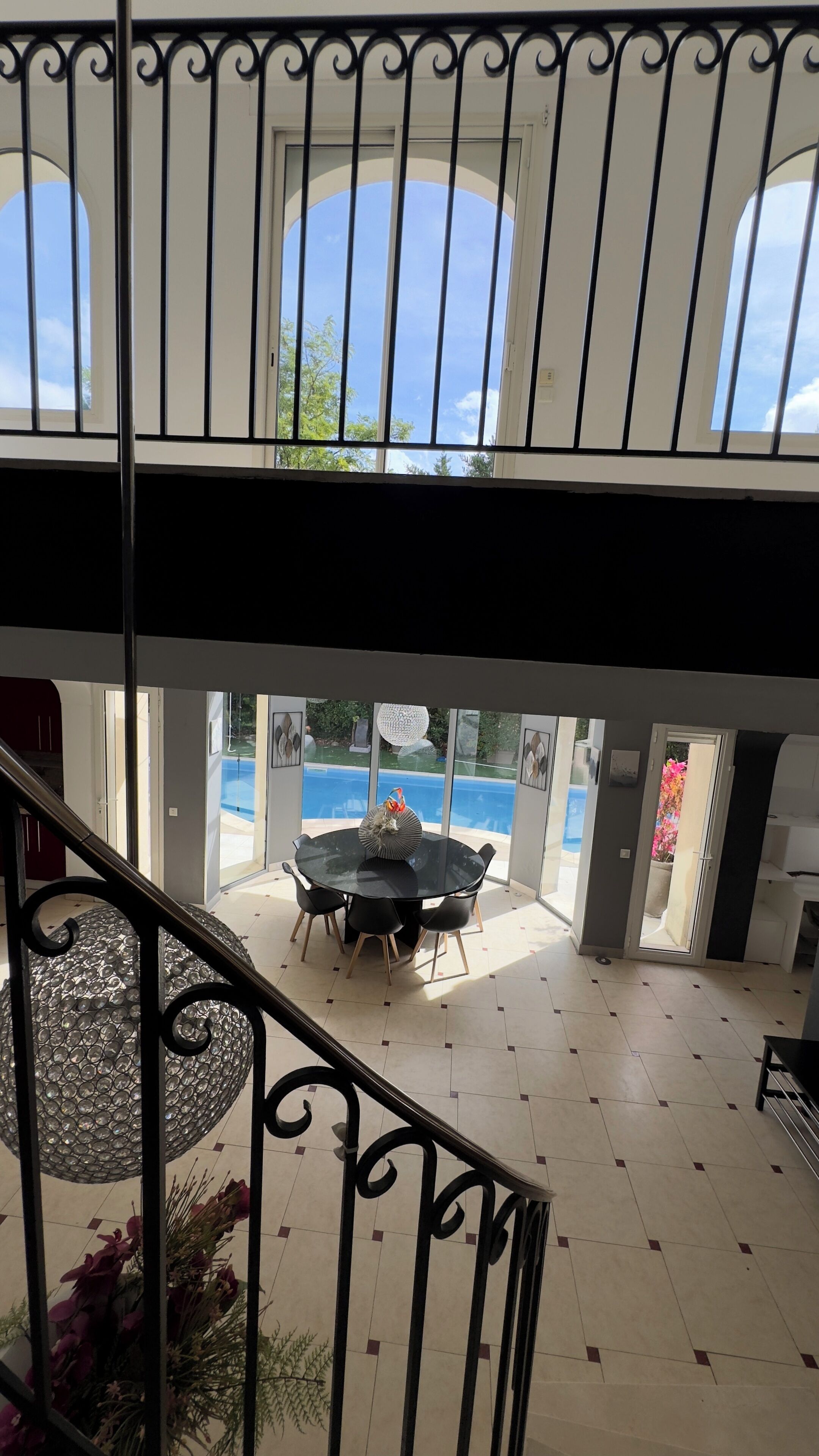 A view from a balcony with a pool and dining area visible through large windows.