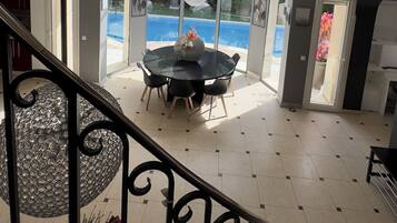 A view from a balcony with a pool and dining area visible through large windows.