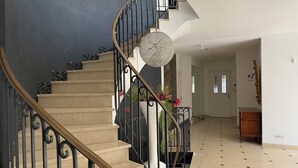 Un interior espacioso con una escalera curva, una araña y vistas al salón.