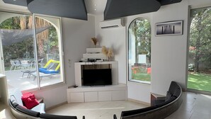 Una sala de estar moderna con una zona de estar curva, un televisor de pantalla plana y ventanas amplias que ofrecen vistas al exterior.
