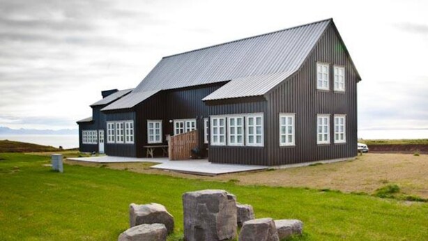 A modern two-story house with a metal roof, large windows, and a grassy yard with rocks. - Day Dream Hellnar (Hellnar)