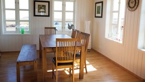 A dining area with a wooden table and chairs, large windows, and framed pictures on the walls. - Day Dream Hellnar (Hellnar)