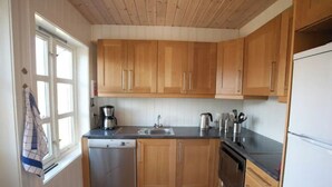 A compact kitchen with wooden cabinets, a dishwasher, a refrigerator, and a window with a towel hanging. - Day Dream Hellnar (Hellnar)