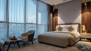 Una camera d'albergo moderna con un letto grande, un angolo salotto con un tavolo e vista sulla città attraverso ampie finestre.