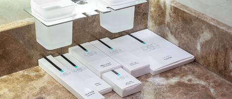 A bathroom with a marble countertop, a glass soap dish, and several toiletries in white boxes.