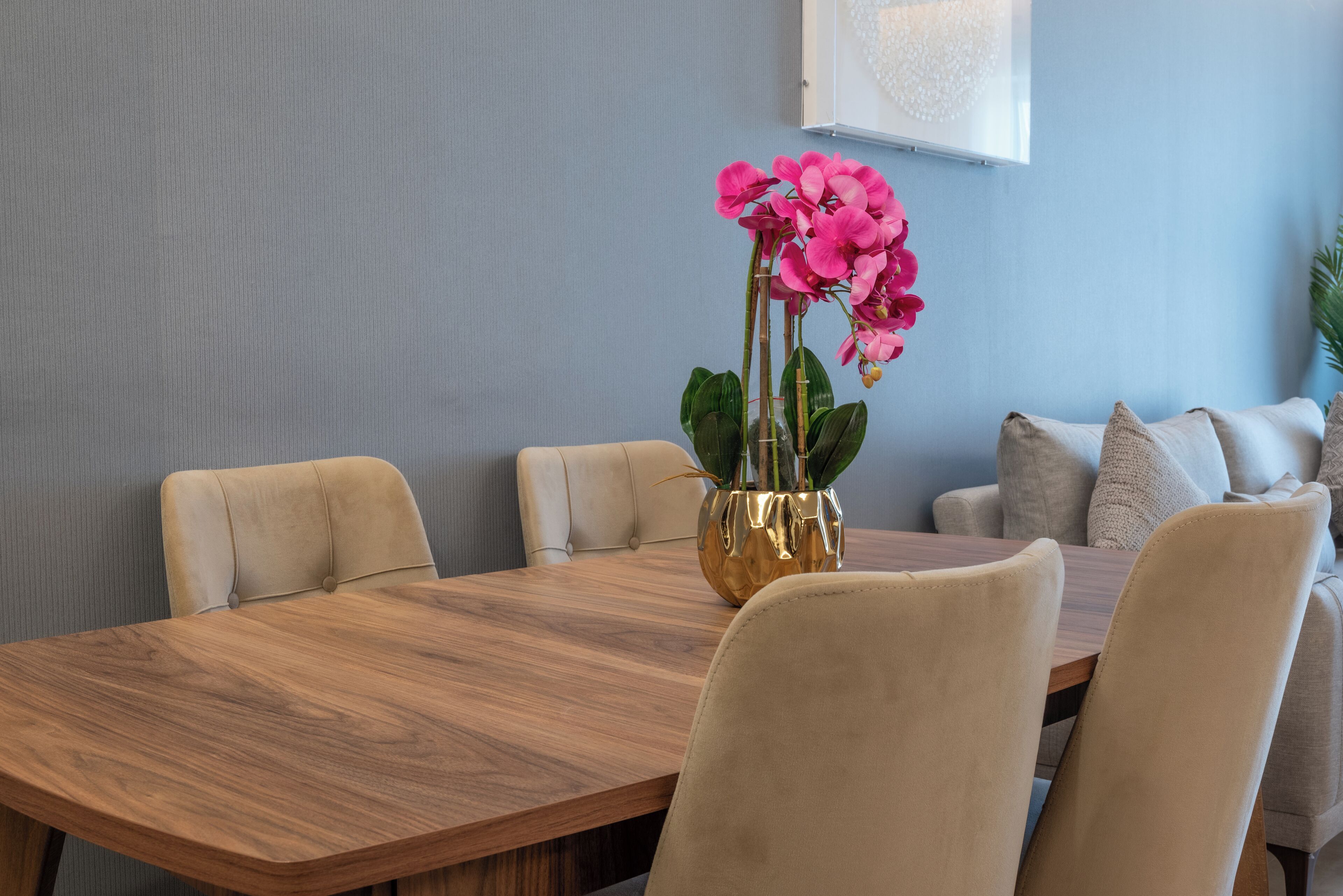 Een eetruimte met een houten tafel, beige stoelen en een vaas met roze bloemen.