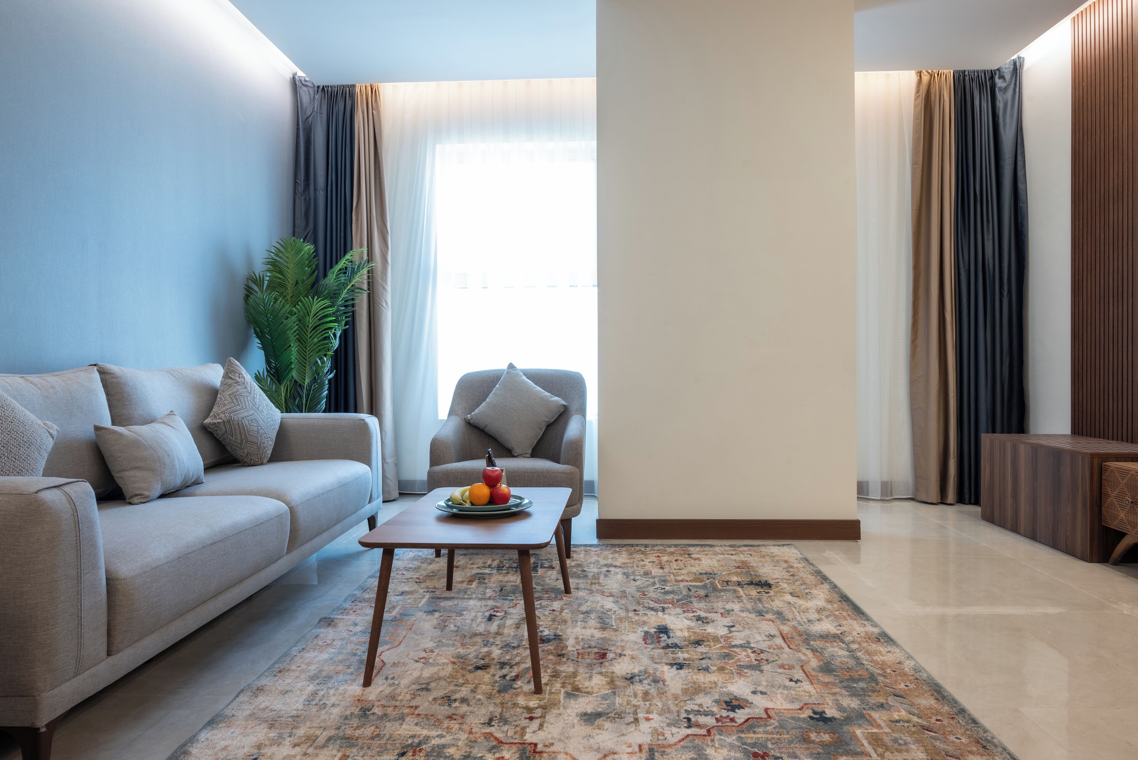 A living room with a sofa, armchair, coffee table, and a plant.