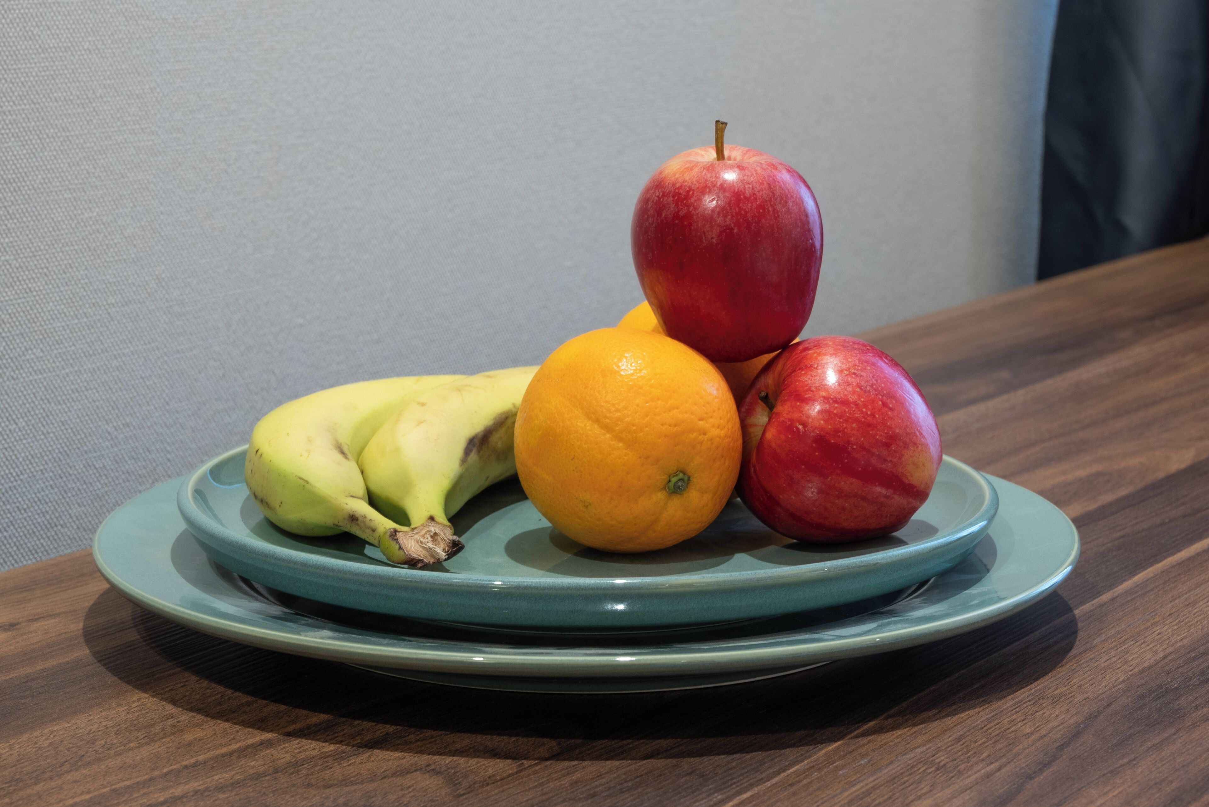 A plate with bananas, an orange, and apples on a wooden table.