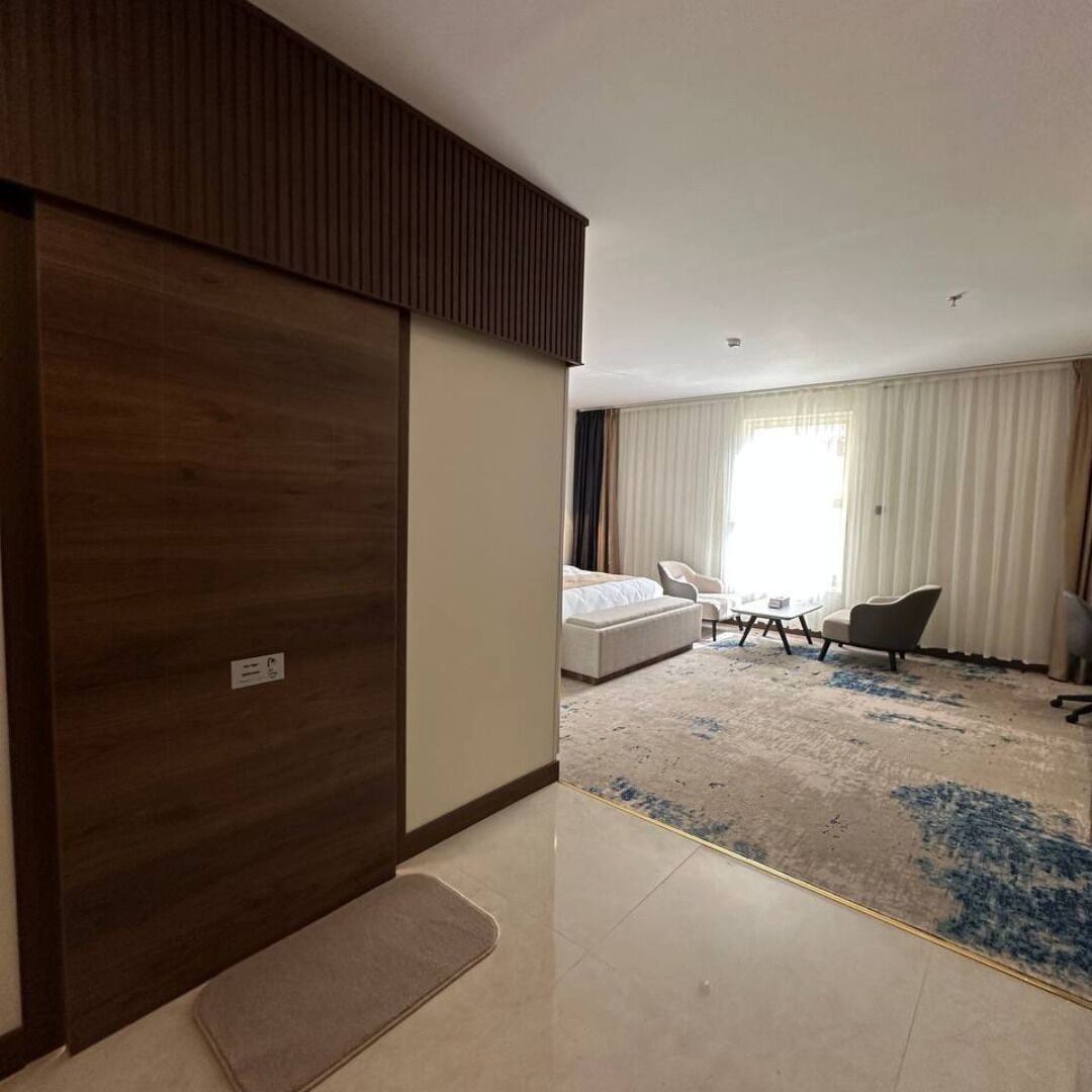 A hotel room with a large wardrobe, a bed, a sofa, a chair, and a small table.