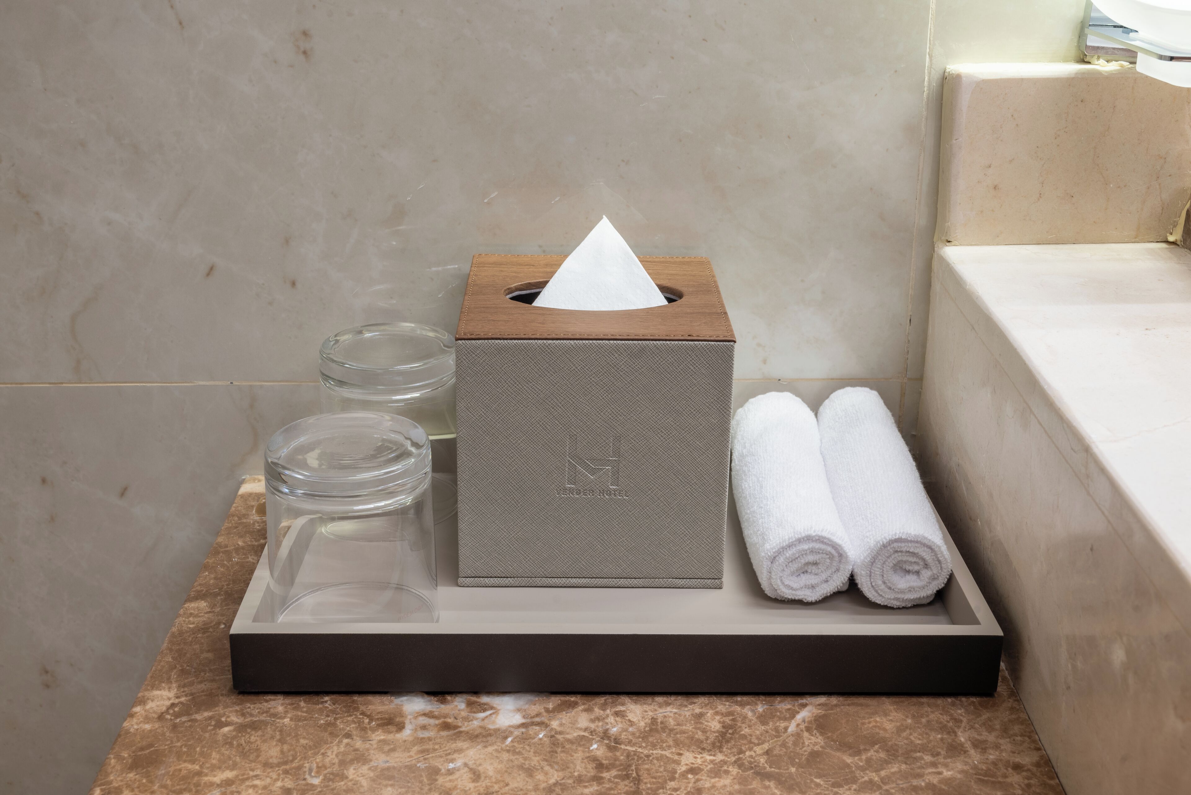 Un meuble-lavabo de salle de bain avec un boîte à mouchoirs, un récipient en verre et deux serviettes enroulées.