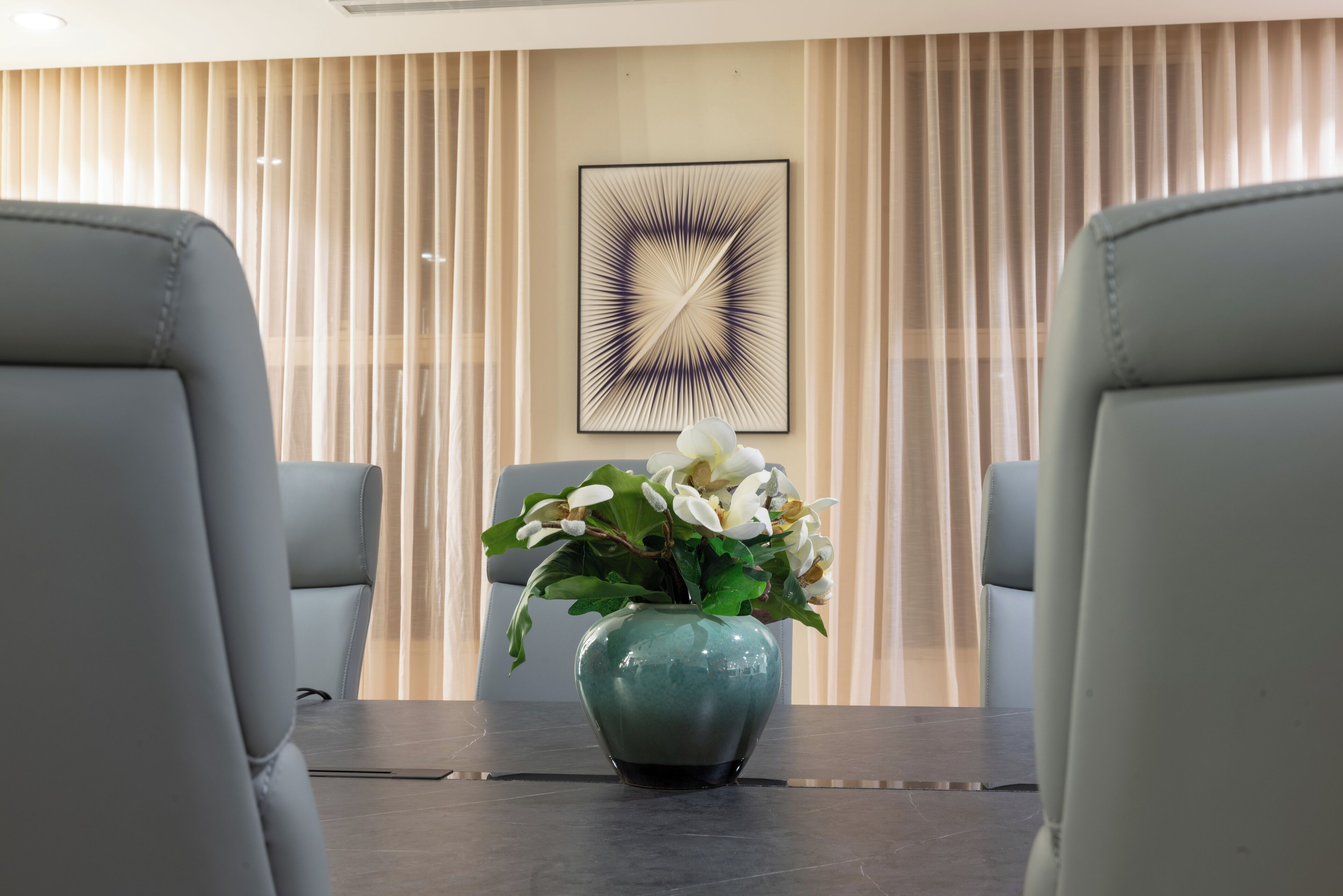 A modern room with a dark wooden table, two grey leather chairs, and a vase with white flowers.