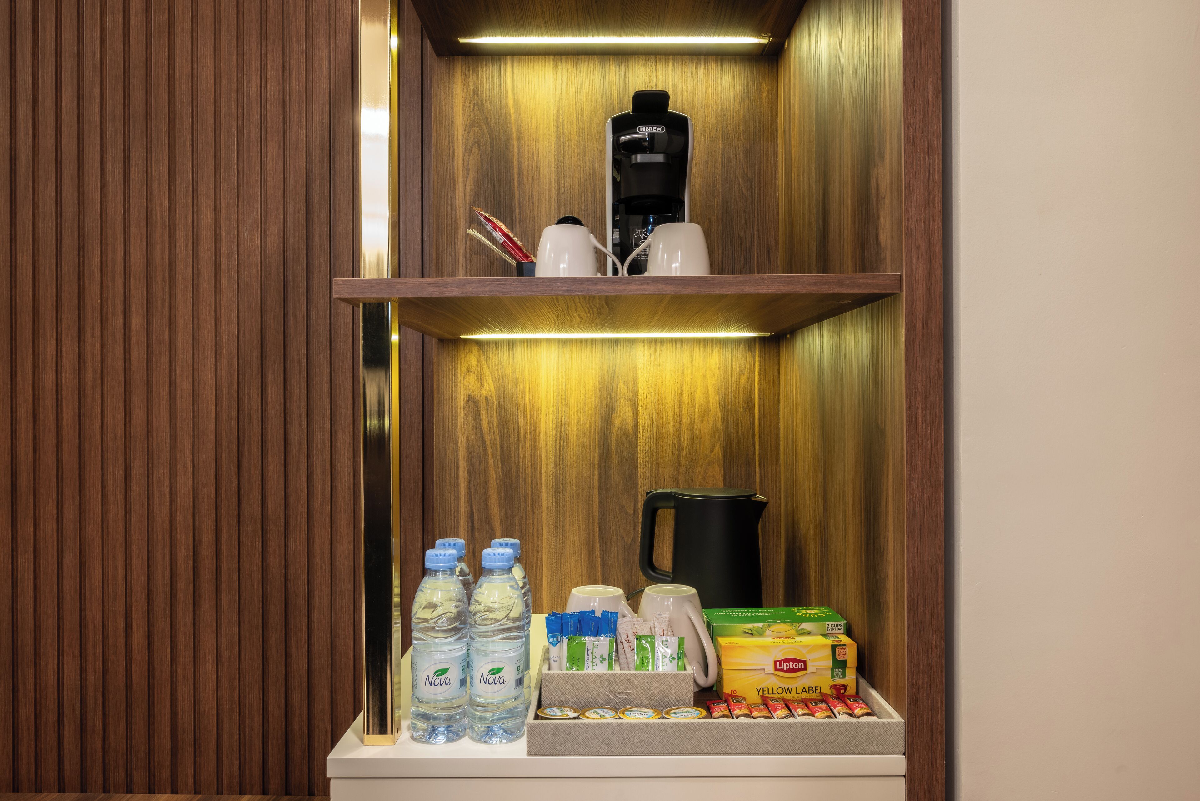 Un mueble de madera con cafetera, botellas de agua, hervidor y una caja de té Lipton.