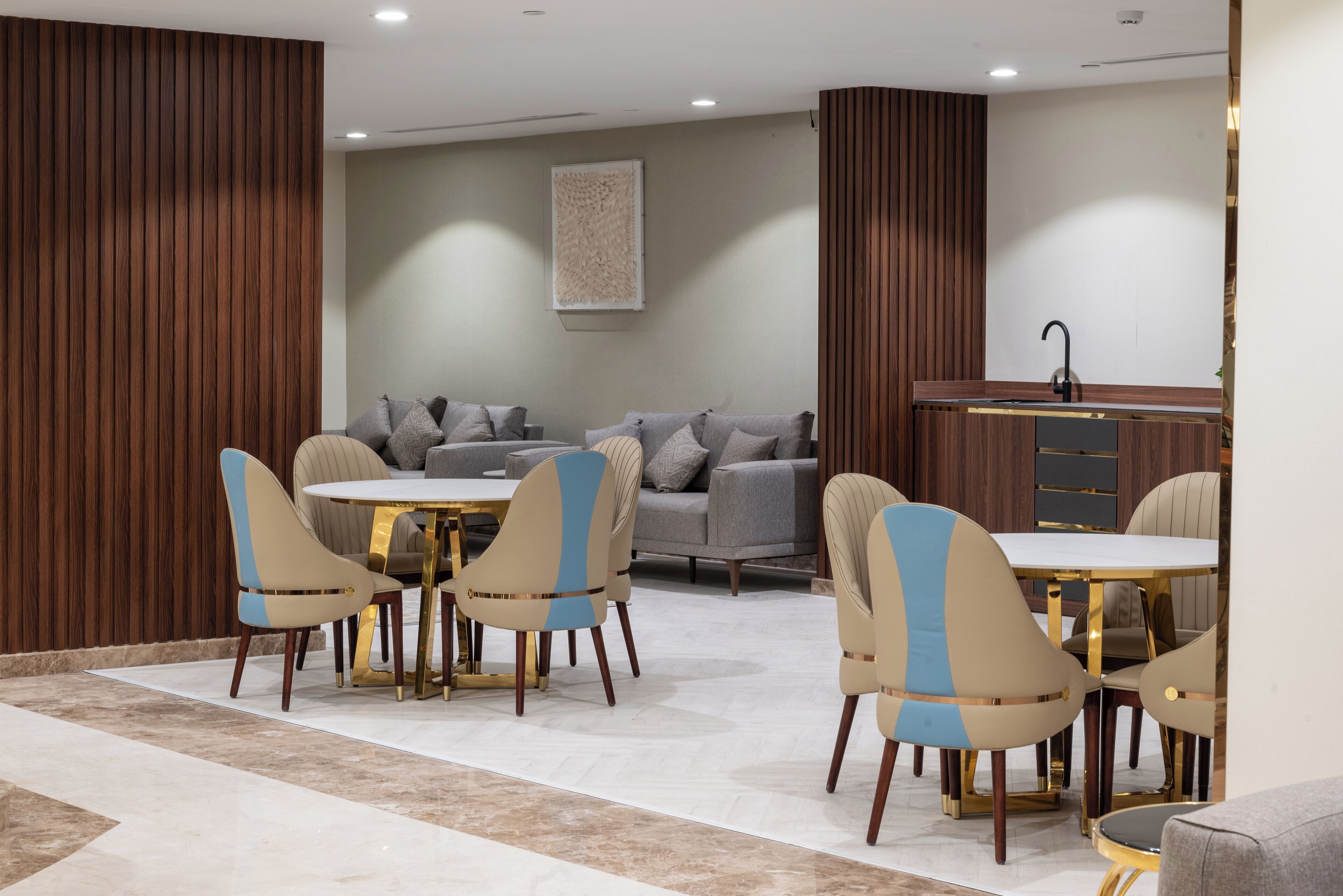 A modern dining area with round tables and chairs, a grey sofa, and a wooden accent wall.